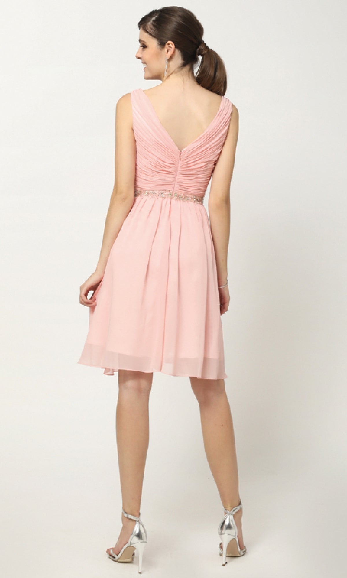A woman faces away, wearing the Juliet 786 short semi-formal dress—a sleeveless, light pink A-line style with V-back and V-neckline—paired with silver high-heeled sandals.